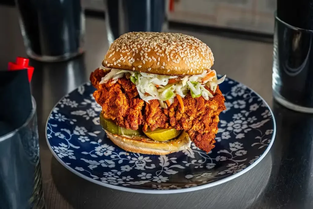 Crispy fried chicken sandwich with pickles, coleslaw, on a blue floral plate.