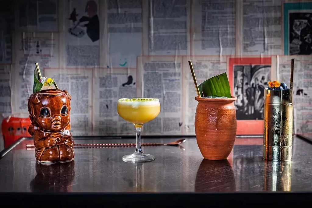 Four unique cocktails in diverse vessels on a dark bar surface.
