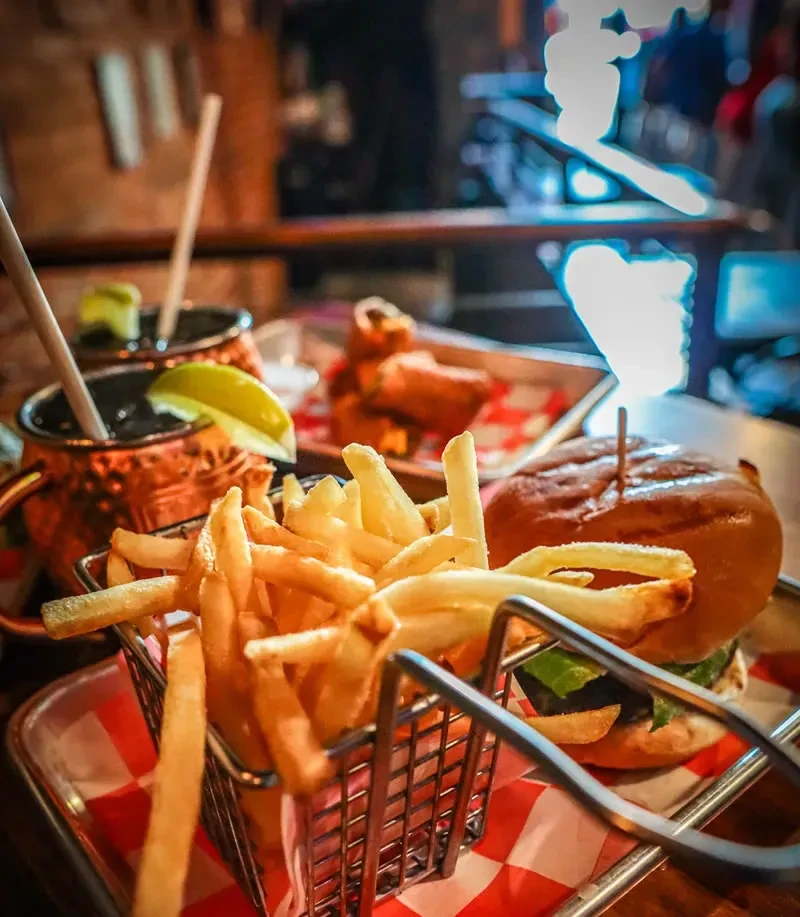 Burger, french fries, and two copper mugs on a checkered tray.