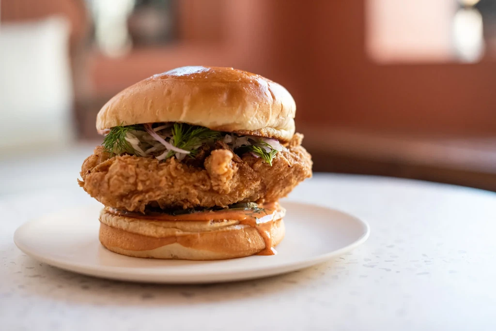 Crispy fried chicken sandwich on a plate with slaw and spicy sauce.
