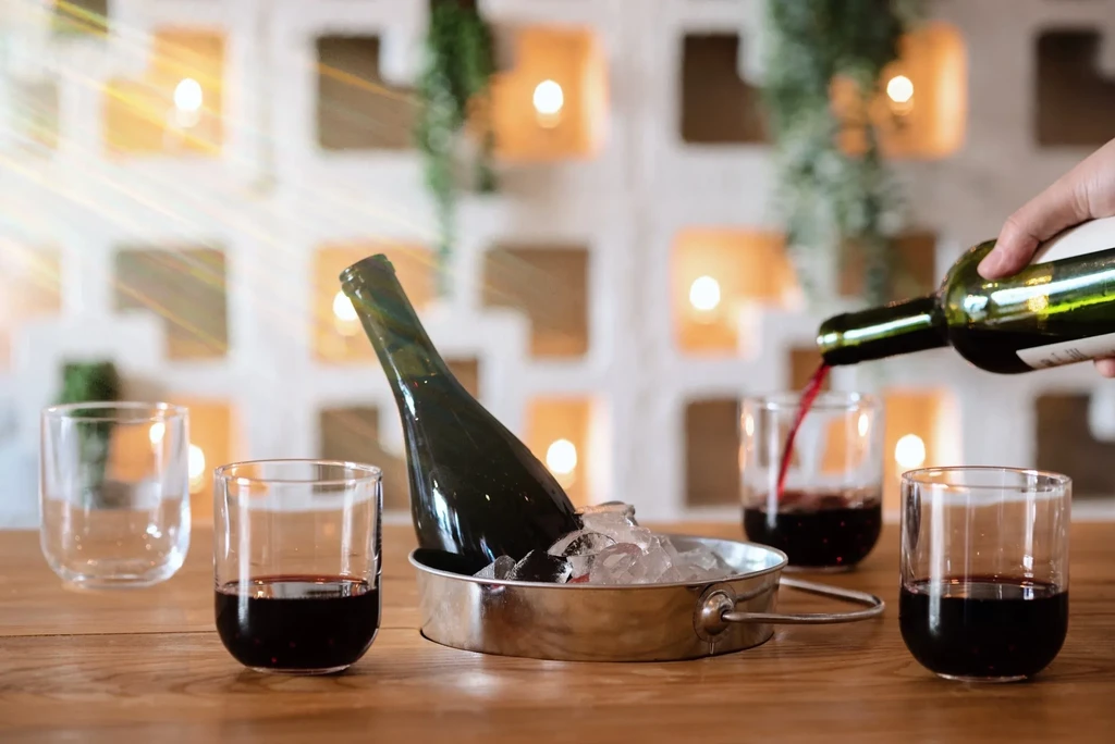 Hand pours red wine into stemless glasses; bottle in ice bucket.