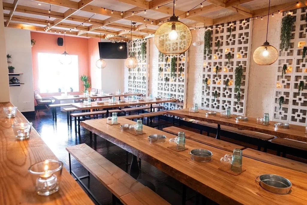 Empty modern rustic restaurant with wooden tables, string lights, and plants.