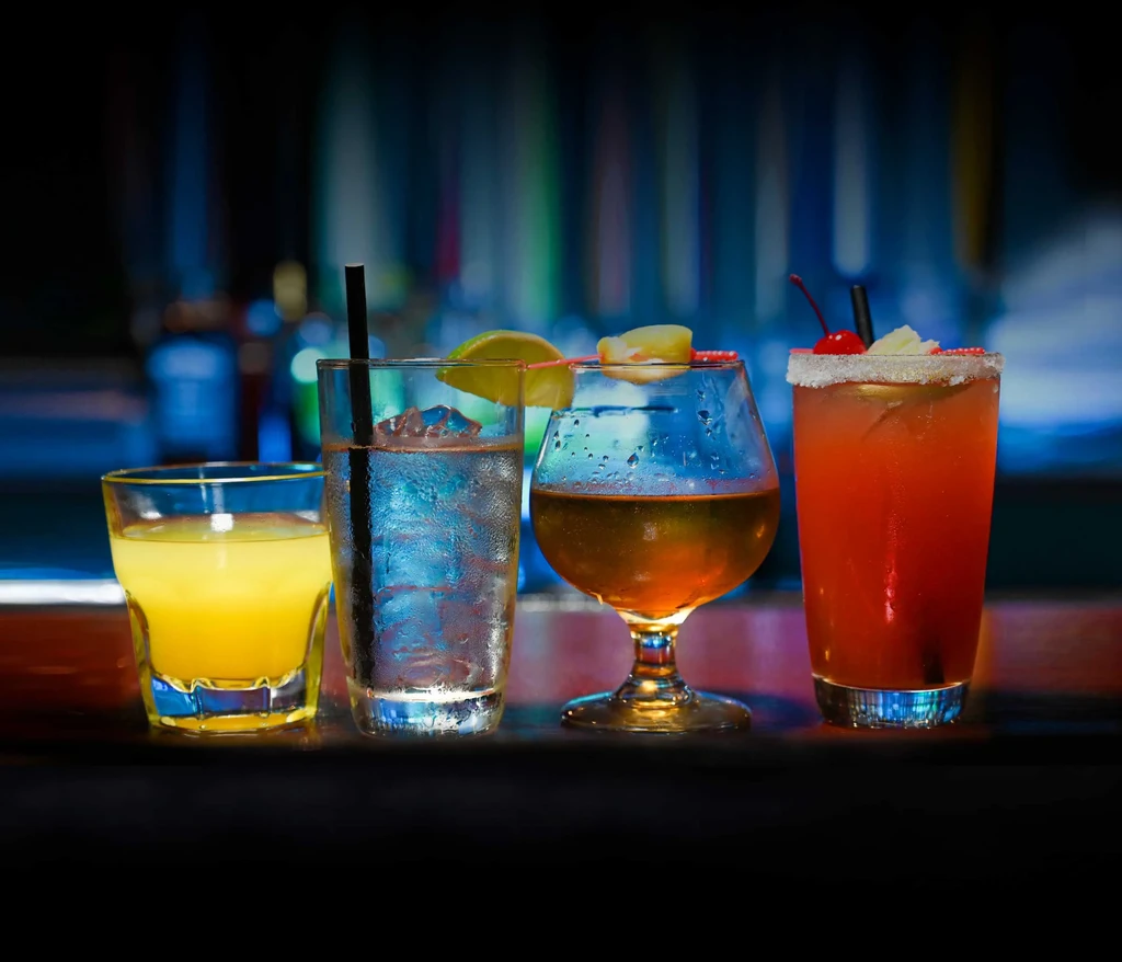 Four distinct cocktails with garnishes on a reflective bar counter.