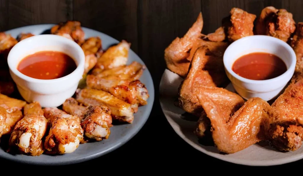 Two plates of golden-brown chicken wings with red dipping sauce.