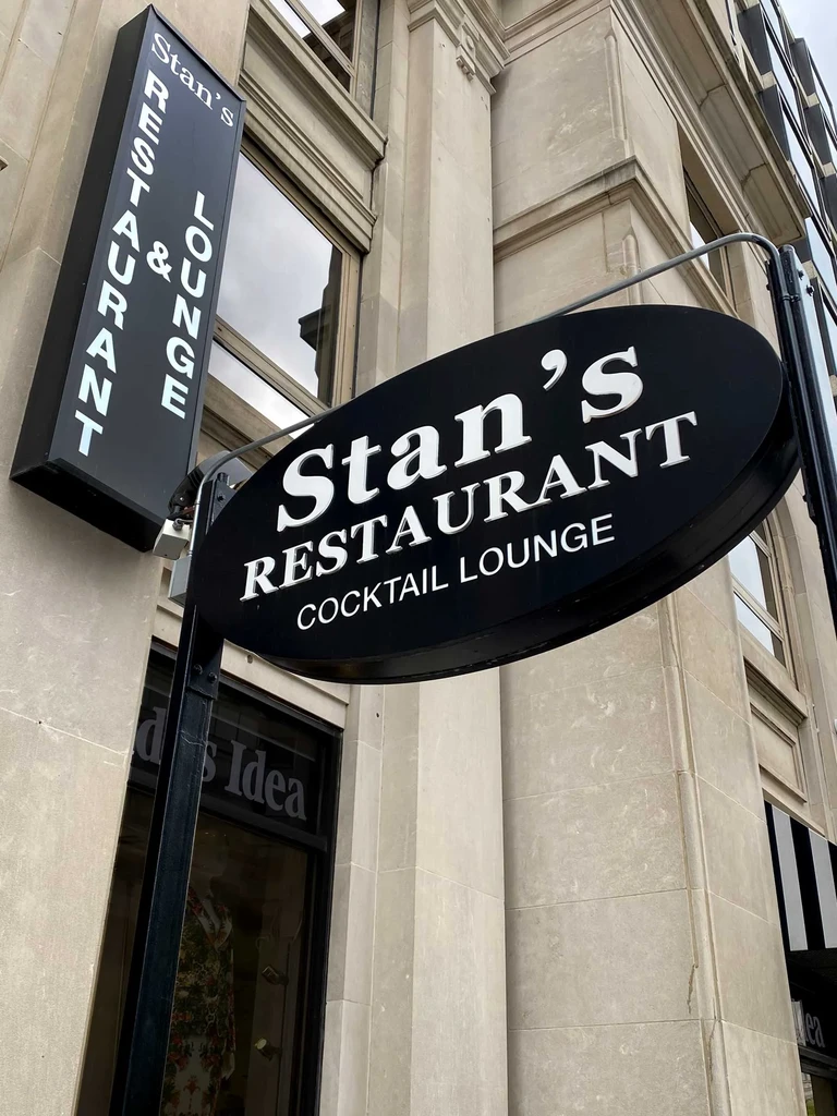 Three black Stan's Restaurant & Lounge signs on a stone building.