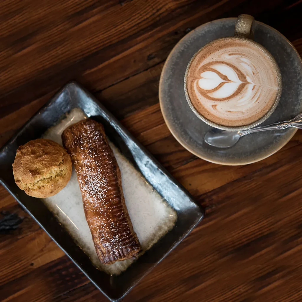 Latte with art, two pastries, and spoon on a wooden table.