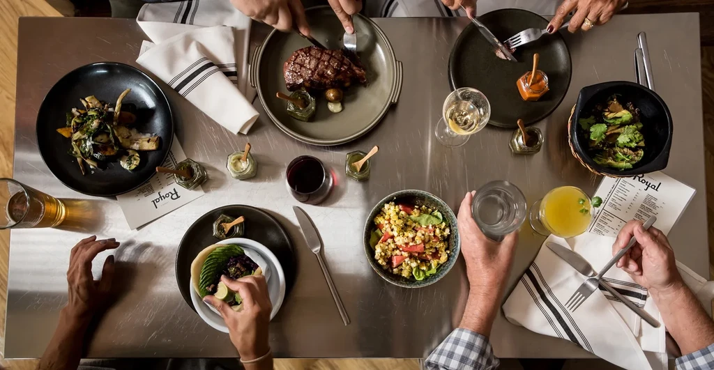 Overhead: Hands reach for steak, drinks, and varied dishes.