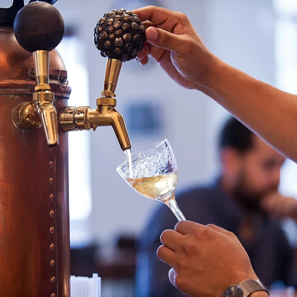 Close-up of hands pouring drink from vintage tap into angled glass.