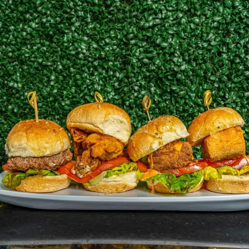 Four diverse sliders on an oval platter with green foliage.