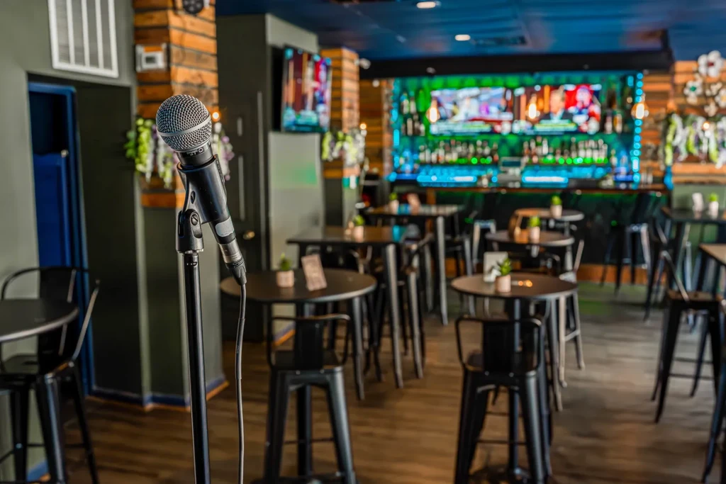 Focused microphone on stage, blurred modern bar with colorful LED lights.