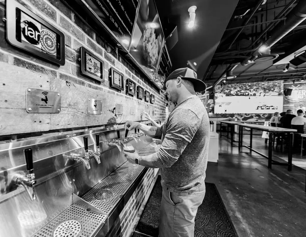 Man pours beer from a tap at a modern self-pour bar.