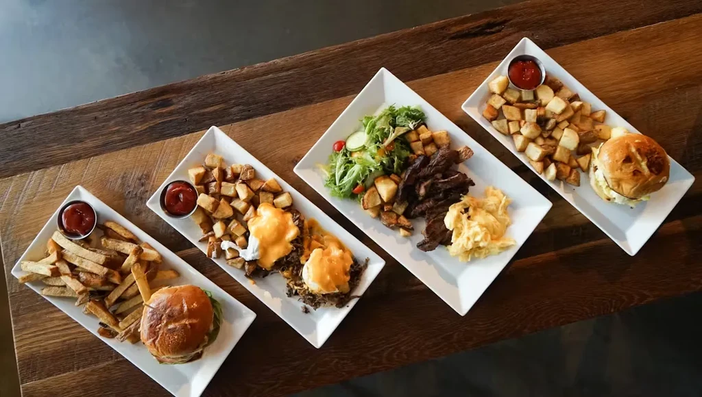 Four distinct meals: burgers, fries, salad, and potatoes on wood.