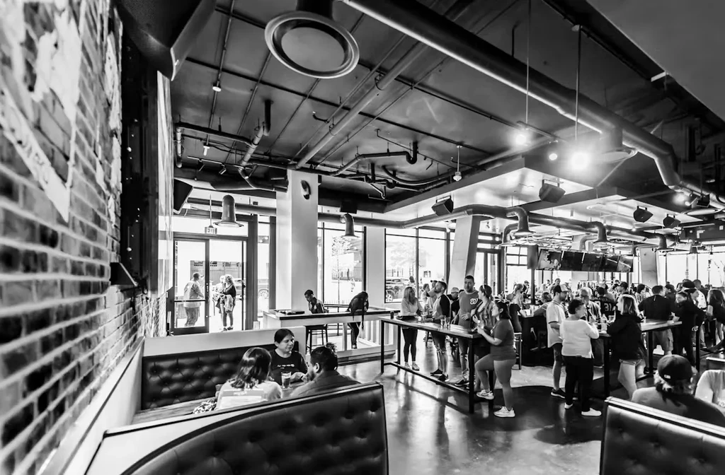 Black and white photo of a busy industrial restaurant interior, full of patrons.