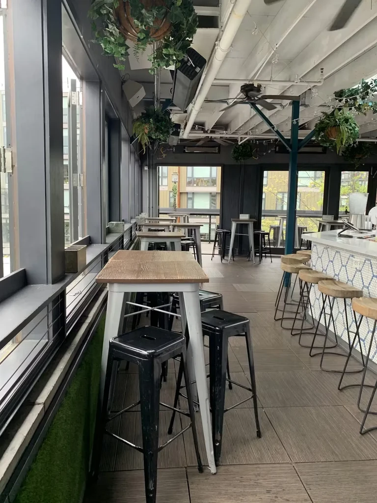 Modern bar/restaurant interior with city view, high-top tables, exposed ceiling.