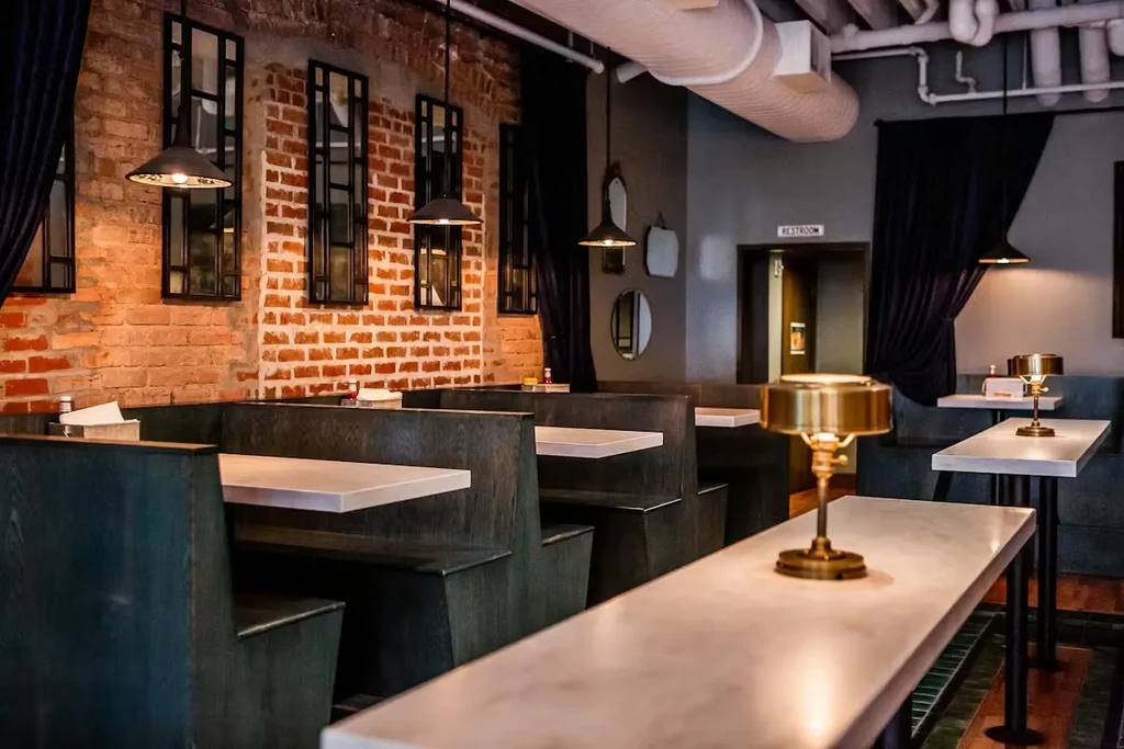 Industrial-chic restaurant interior with brick, booth seating, and art deco lamps.