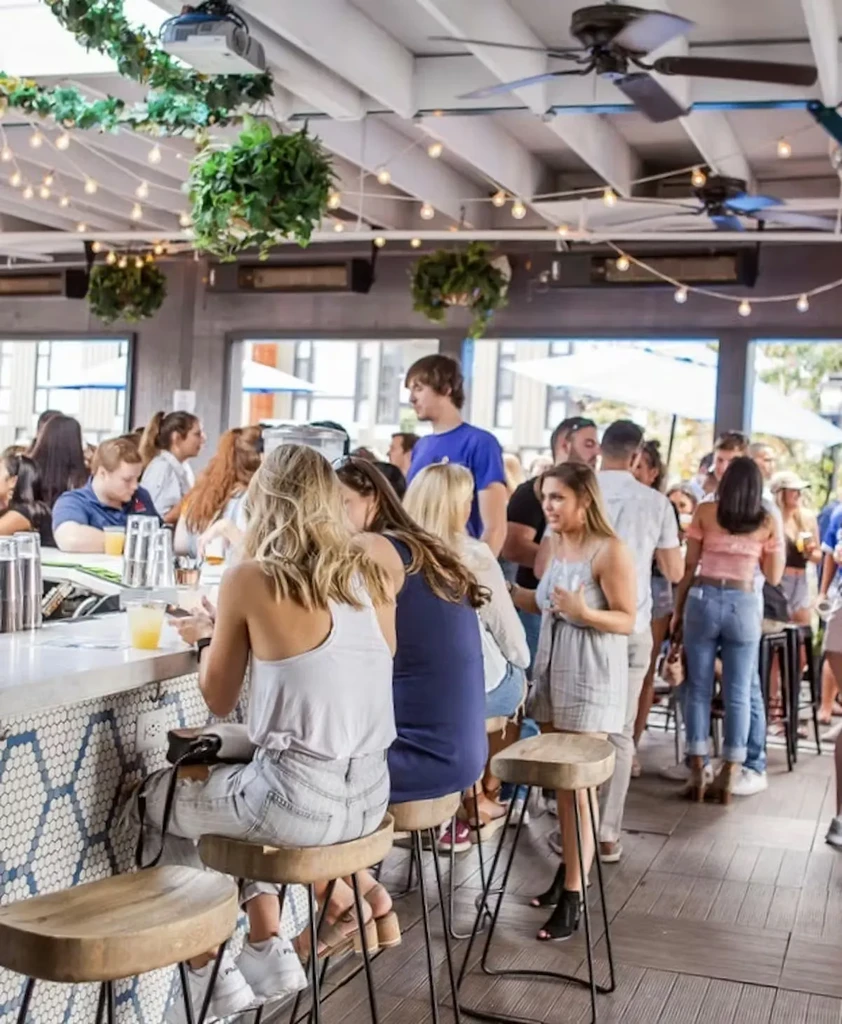 Lively modern bar with people, white counter, plants, and hexagonal wall.