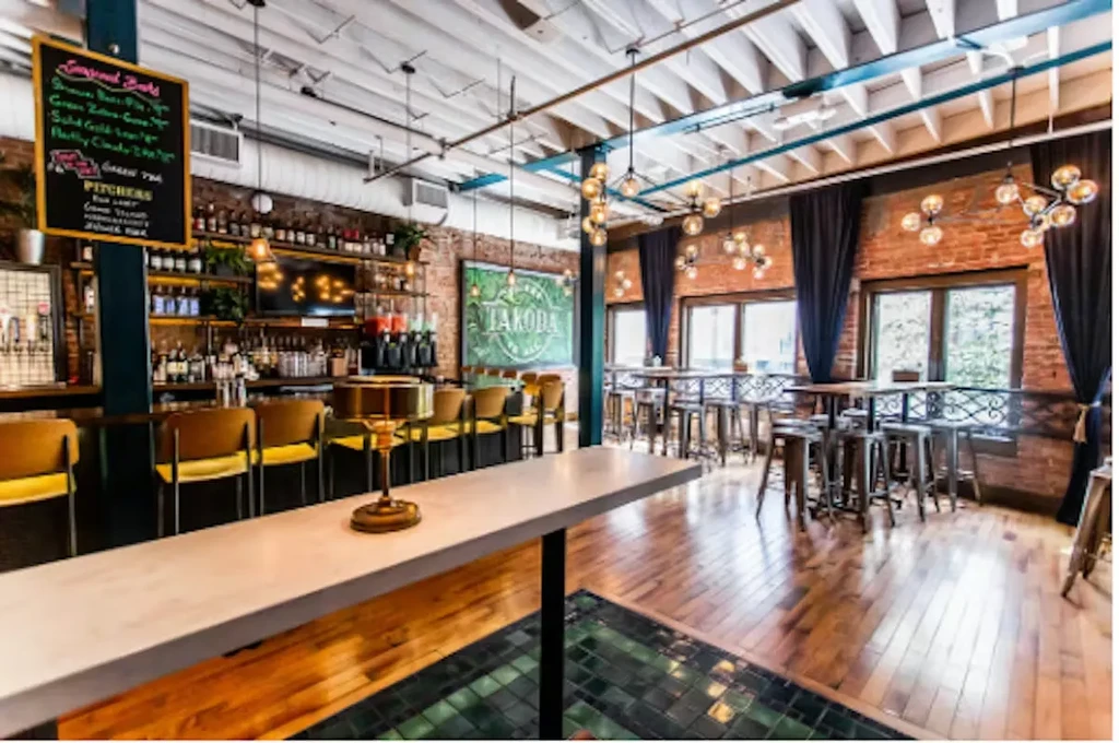 Modern industrial-chic bar interior with exposed brick, long counter, and "TAKOBA" sign.