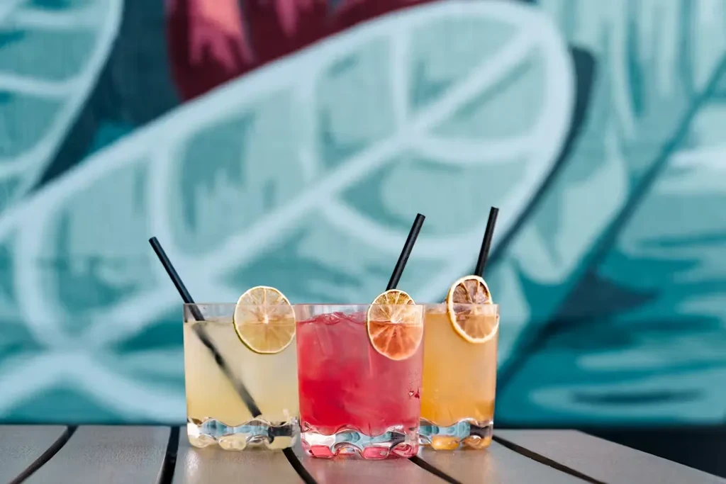 Three vibrant yellow, red, orange drinks with citrus on a wooden table.