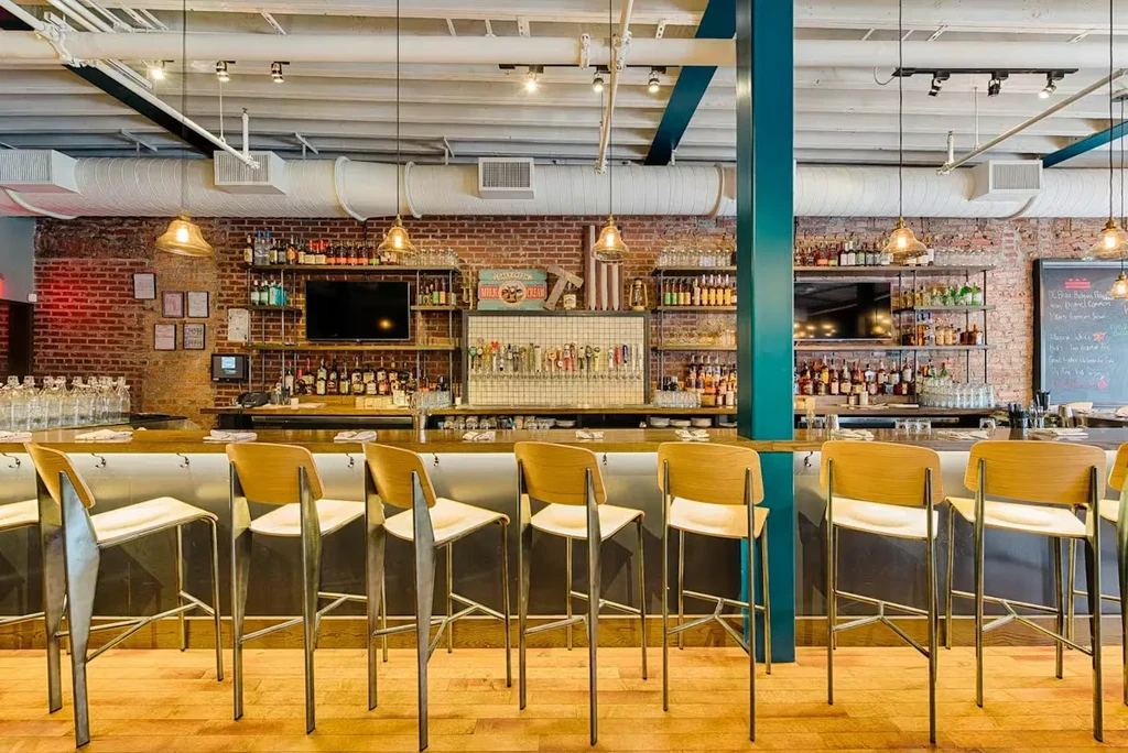 Empty modern bar, brick wall, liquor bottles, beer taps, teal column.