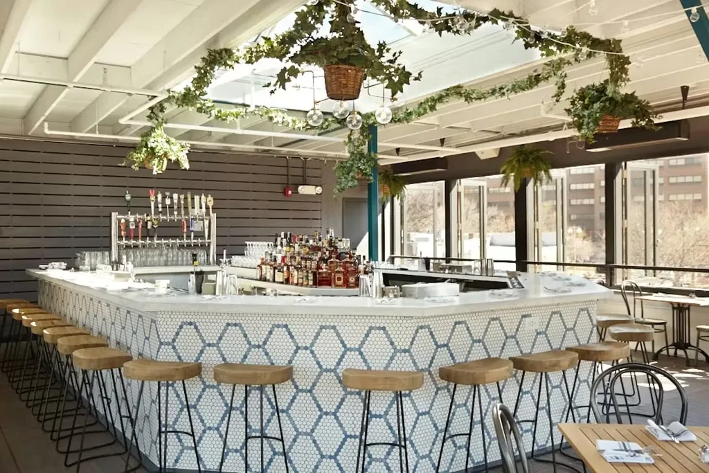 Spacious bar with U-shaped counter, blue hexagonal tiles, liquor, and plants.