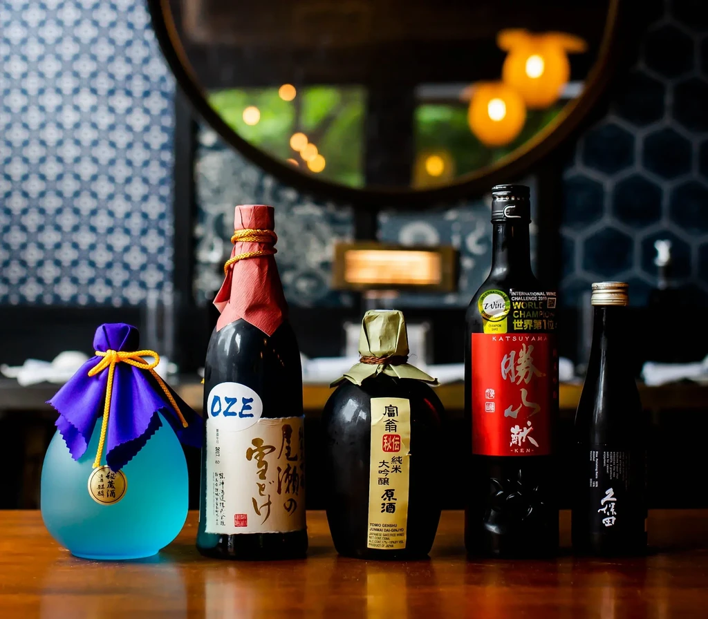 Five distinct sake bottles arranged on a wooden surface.
