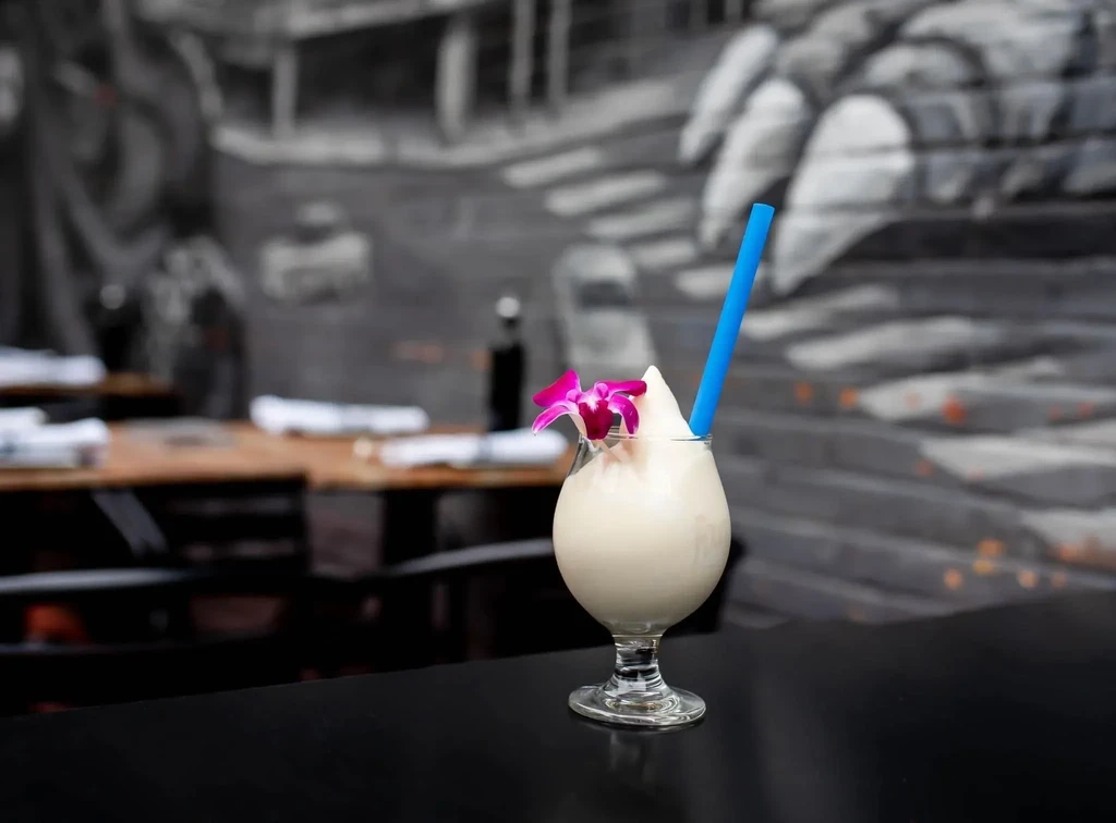 Frozen white cocktail with orchid and blue straw in a restaurant.