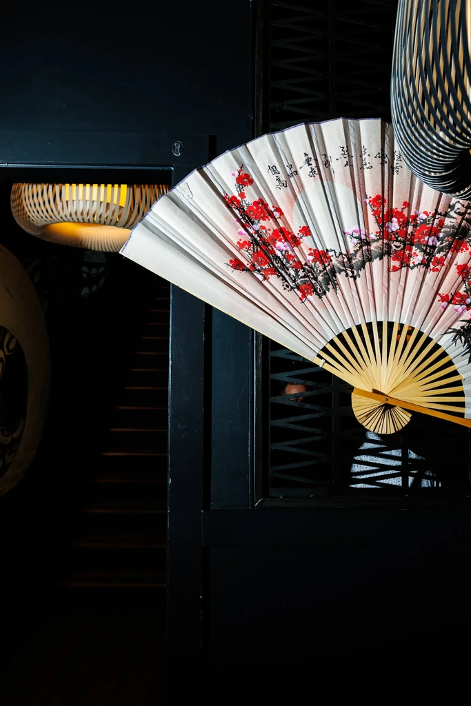 Decorative hand fan with red blossoms and calligraphy, beside a glowing lantern.