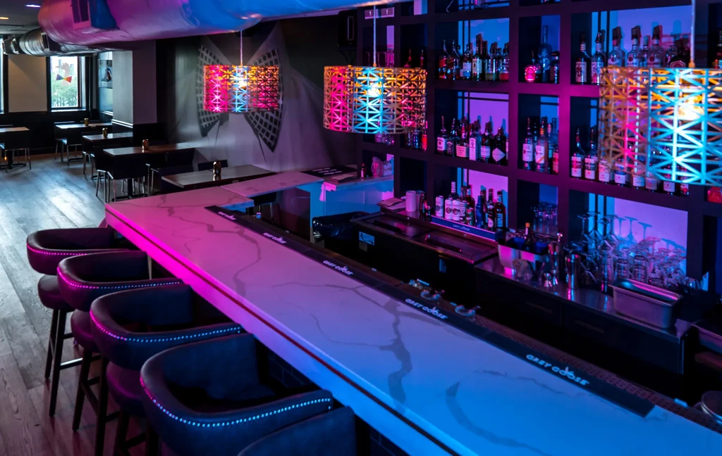 Modern bar with white marbled counter and vibrant pink-blue neon lights.