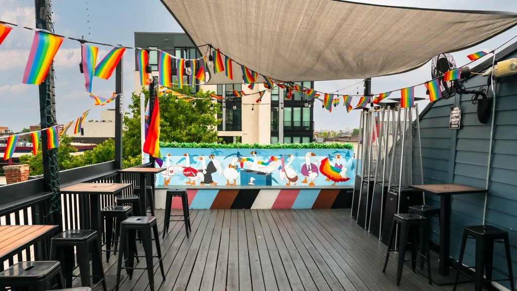 Outdoor patio with high tables, rainbow flags, and anthropomorphic goose mural.