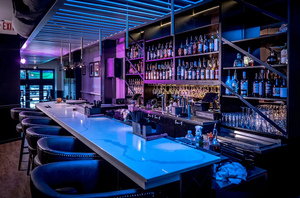 Modern bar interior with blue-lit white marble bar top and liquor shelves.