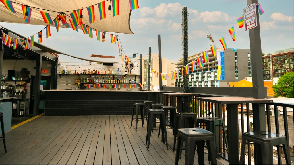 Open-air rooftop bar with pride flags and city skyline.