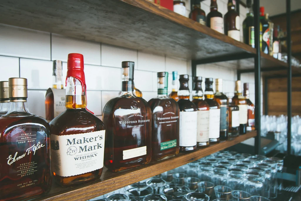 Well-stocked bar shelf with whiskey, bourbon bottles, and stacked glassware.