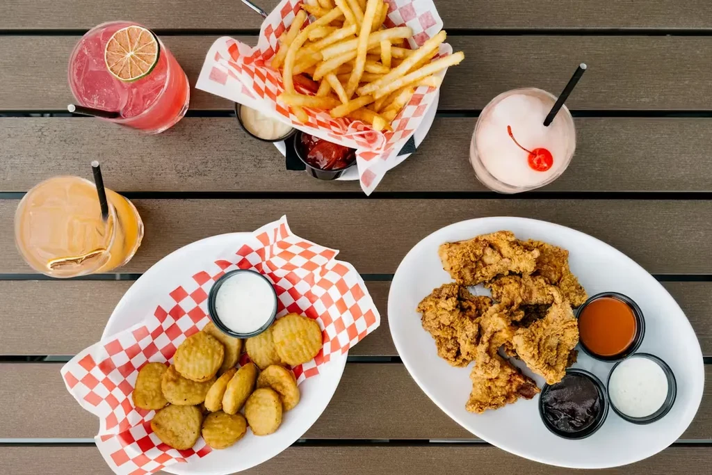 Fried chicken, french fries, appetizers, and four colorful drinks on a table.