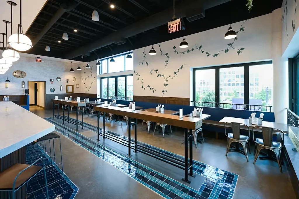 Modern industrial-chic restaurant with bar, communal table, vine mural.