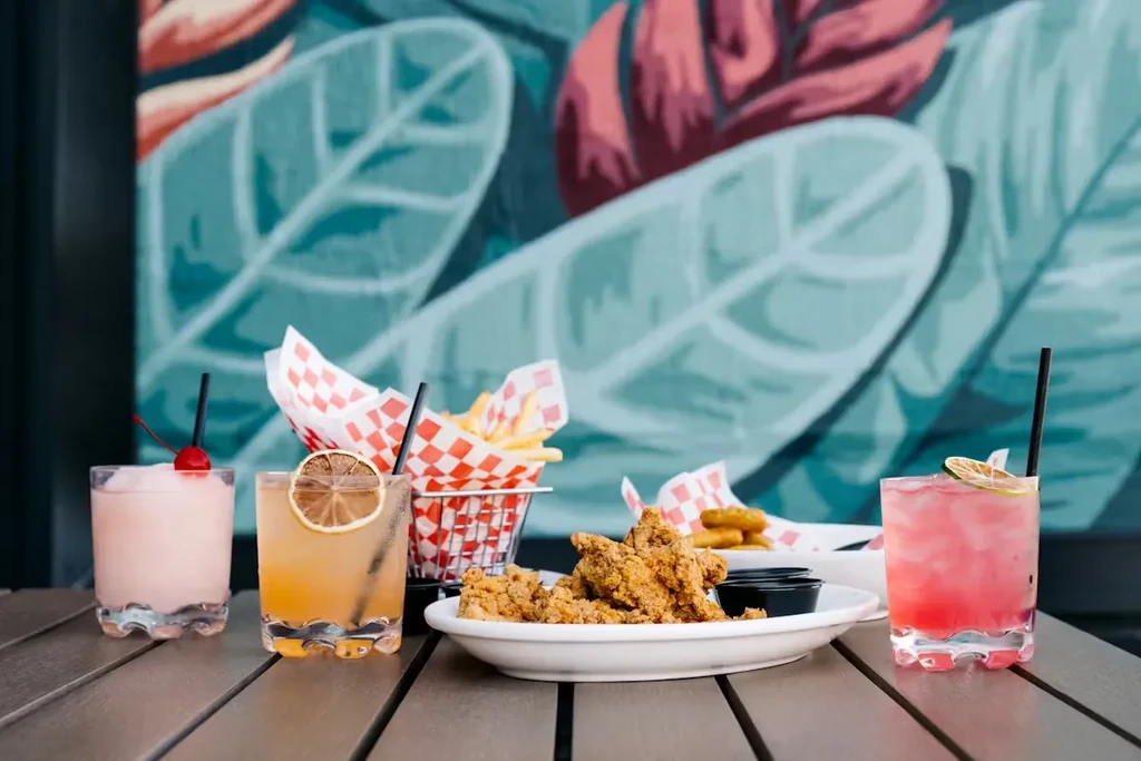 Fried chicken, french fries, and three colorful cocktails on a wooden table.