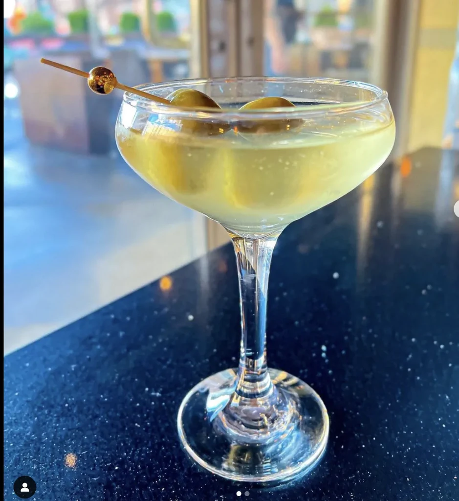 Yellowish-green martini in a coupe glass, garnished with two green olives.