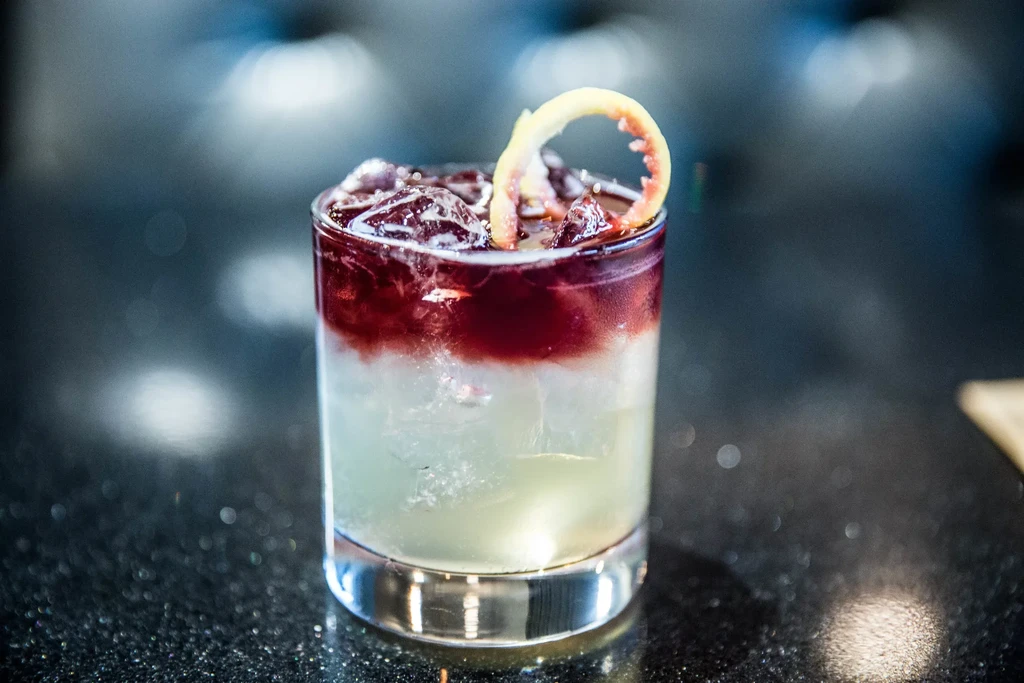 Layered green and red cocktail with ice and citrus peel.