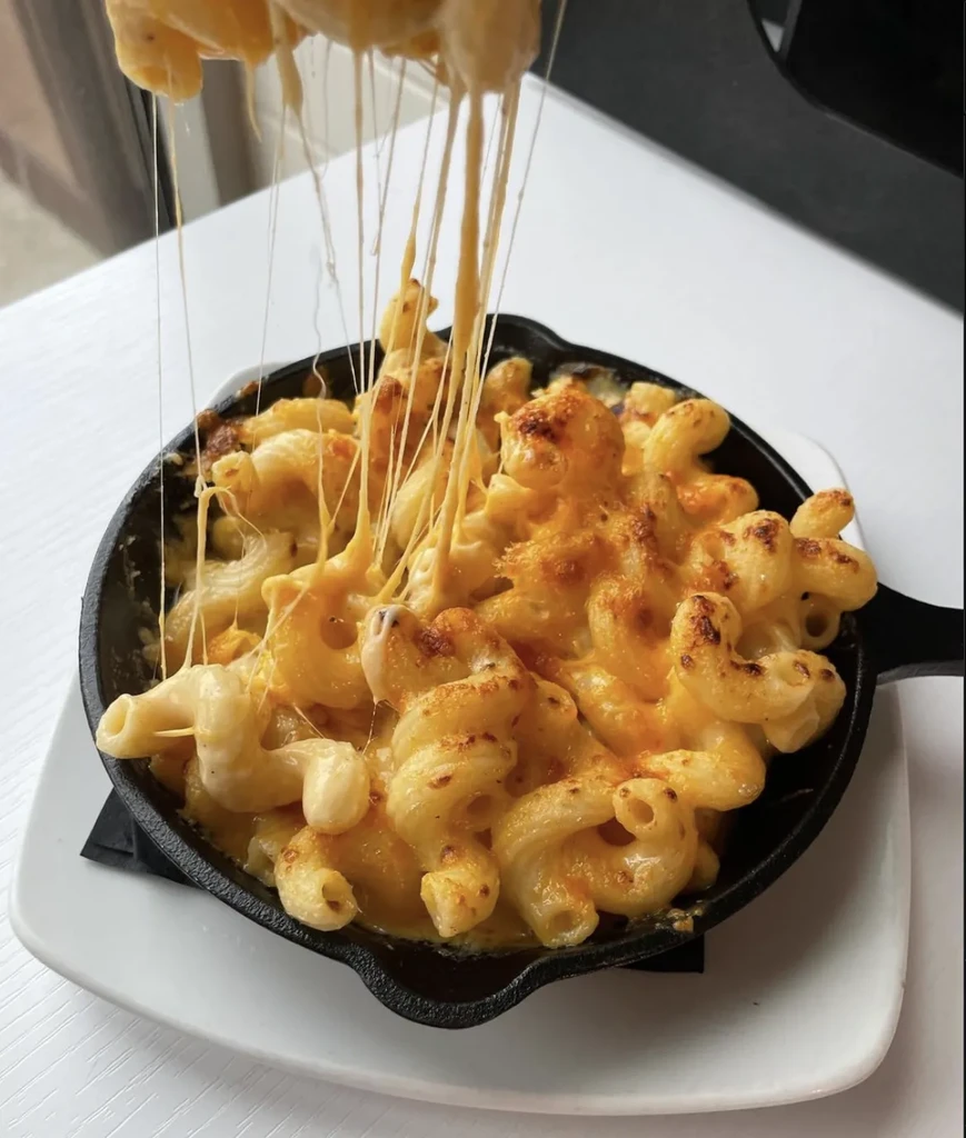 Golden baked mac and cheese lifted from skillet, showing gooey cheese strands.