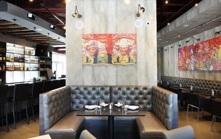Modern restaurant interior with large U-shaped booth, abstract art, and bar.