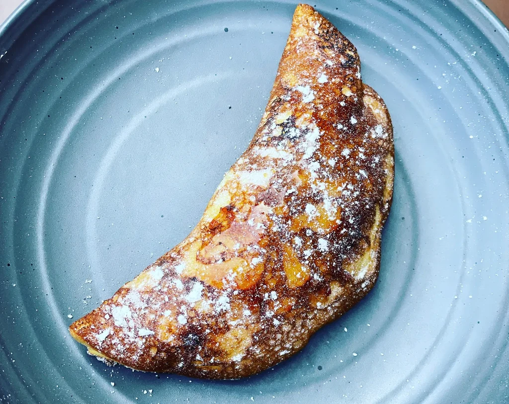 Crescent-shaped turnover dusted with powdered sugar on a plate.