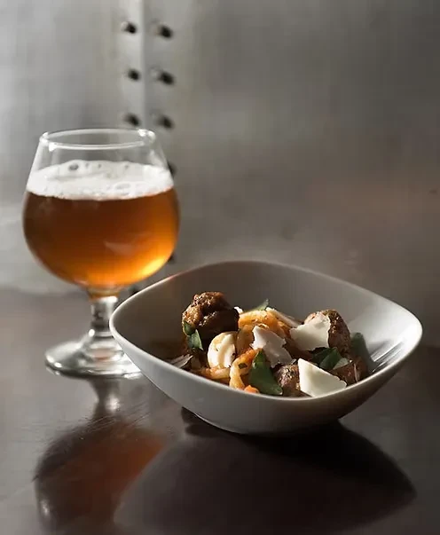 Amber beer in a stemmed glass and a bowl of food.