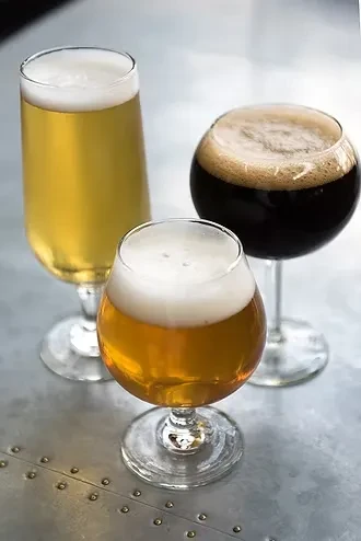 Three glasses of golden, amber, and dark beer on metal.