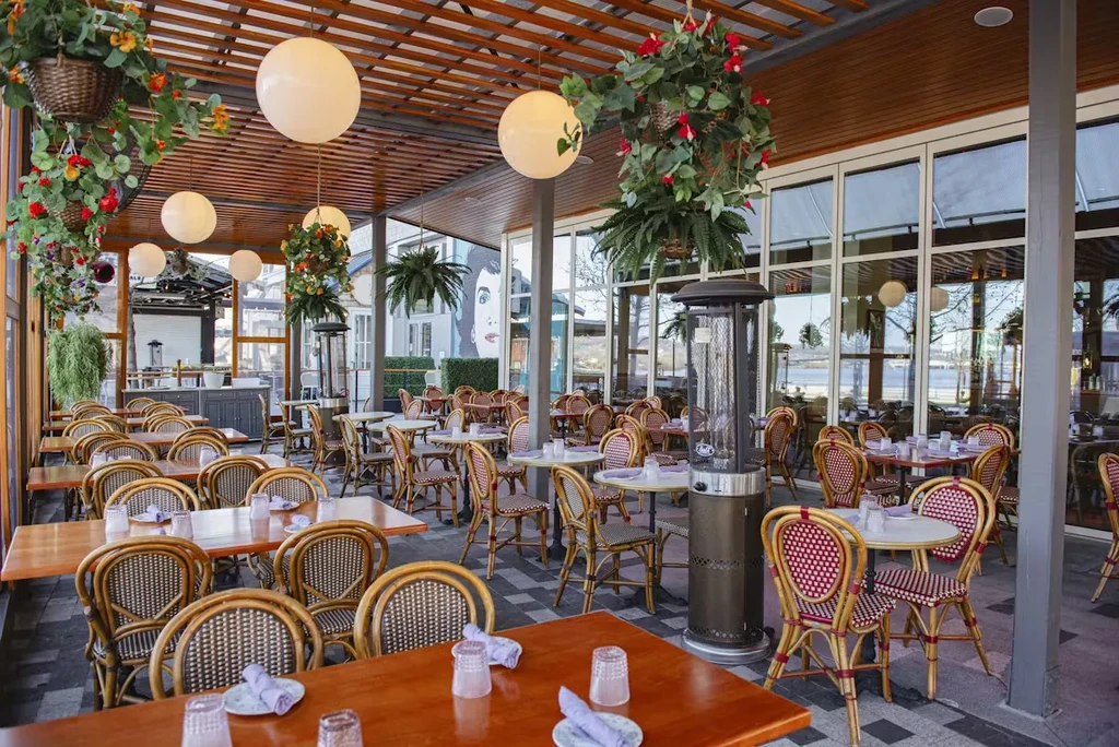 Outdoor patio dining area with wicker chairs, pergola, heaters, and mural.