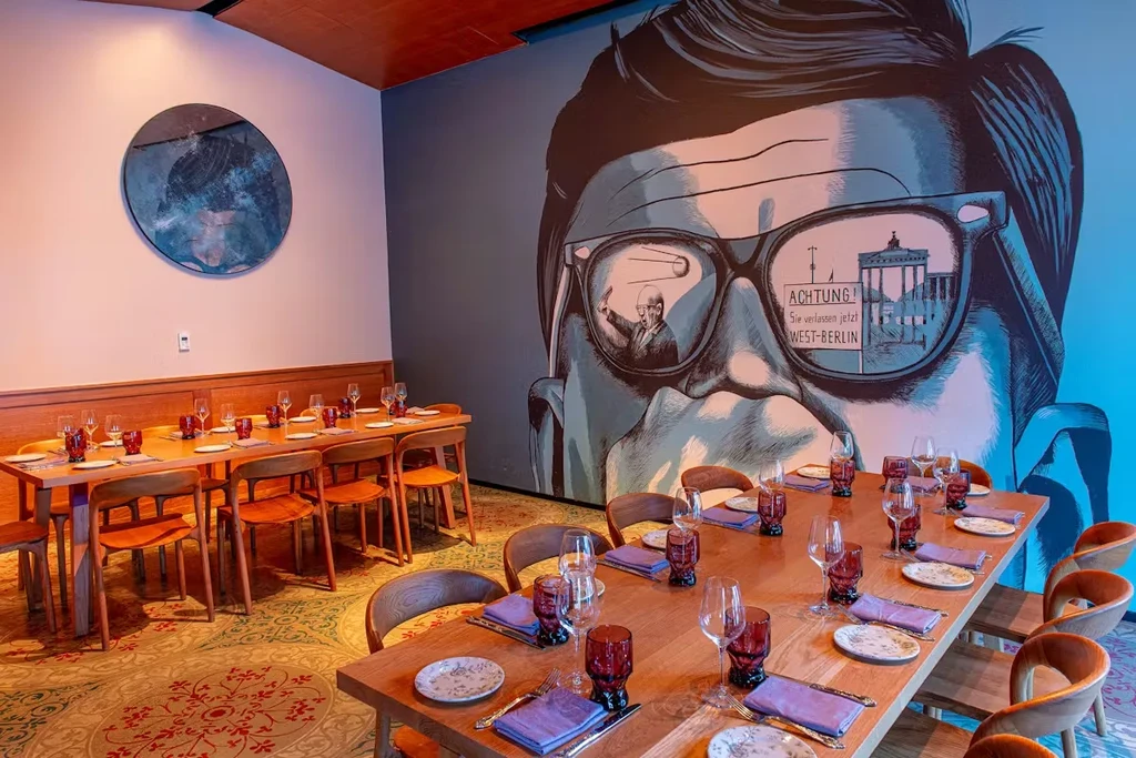 Modern restaurant with set tables, patterned floor, and Berlin-themed mural.