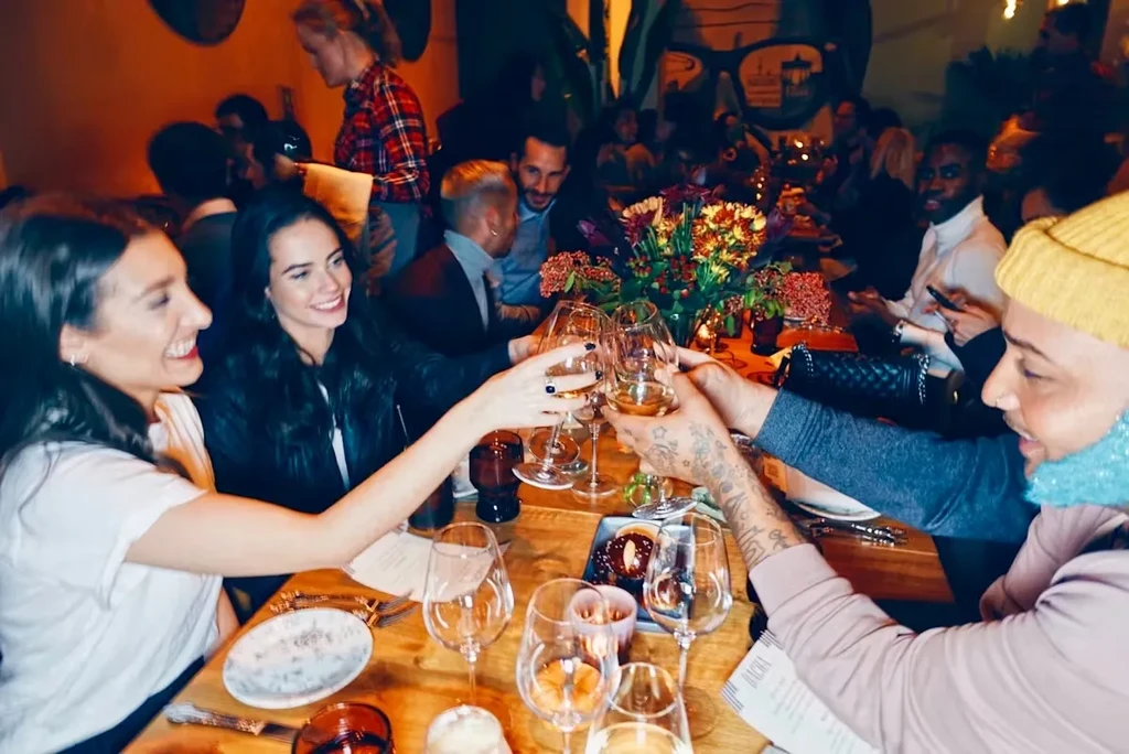 Friends toasting with wine glasses at a dim, lively restaurant.