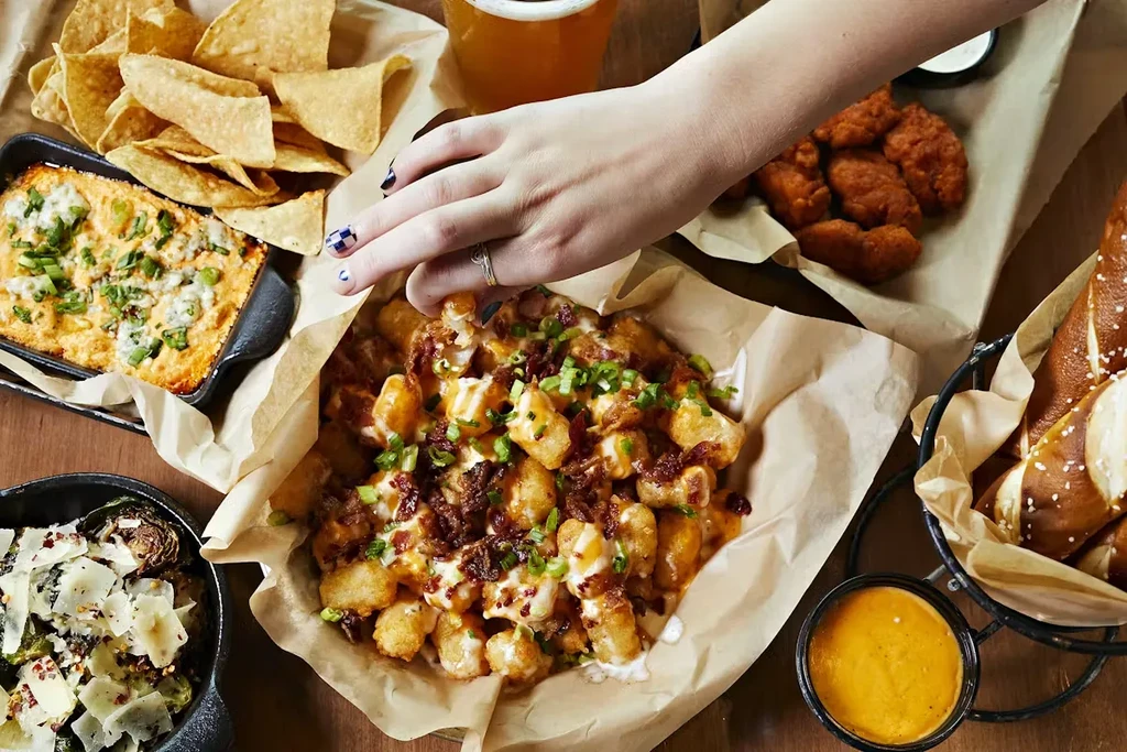 Overhead view: Hand reaches into loaded tater tots with other appetizers.