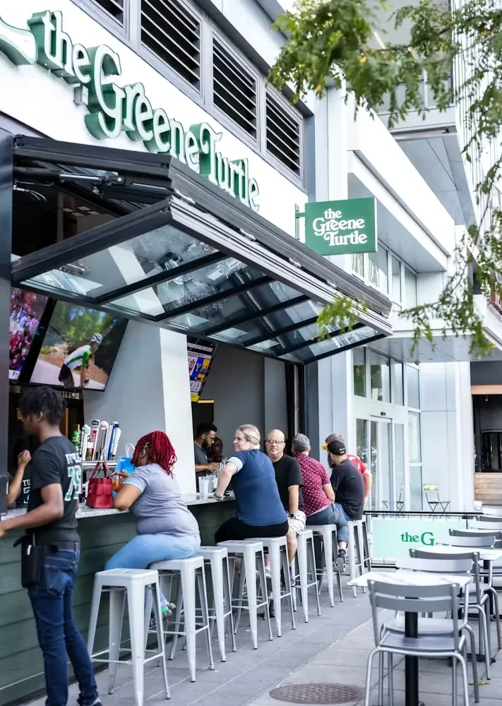 The Greene Turtle outdoor bar with patrons seated at a street-facing counter.