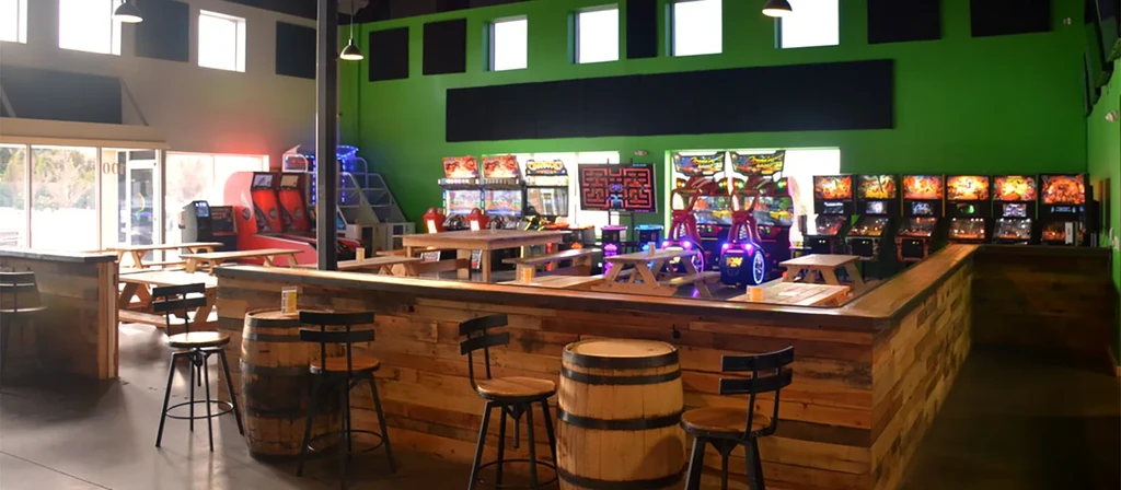 Empty spacious arcade bar with rustic bar, picnic tables, colorful games.