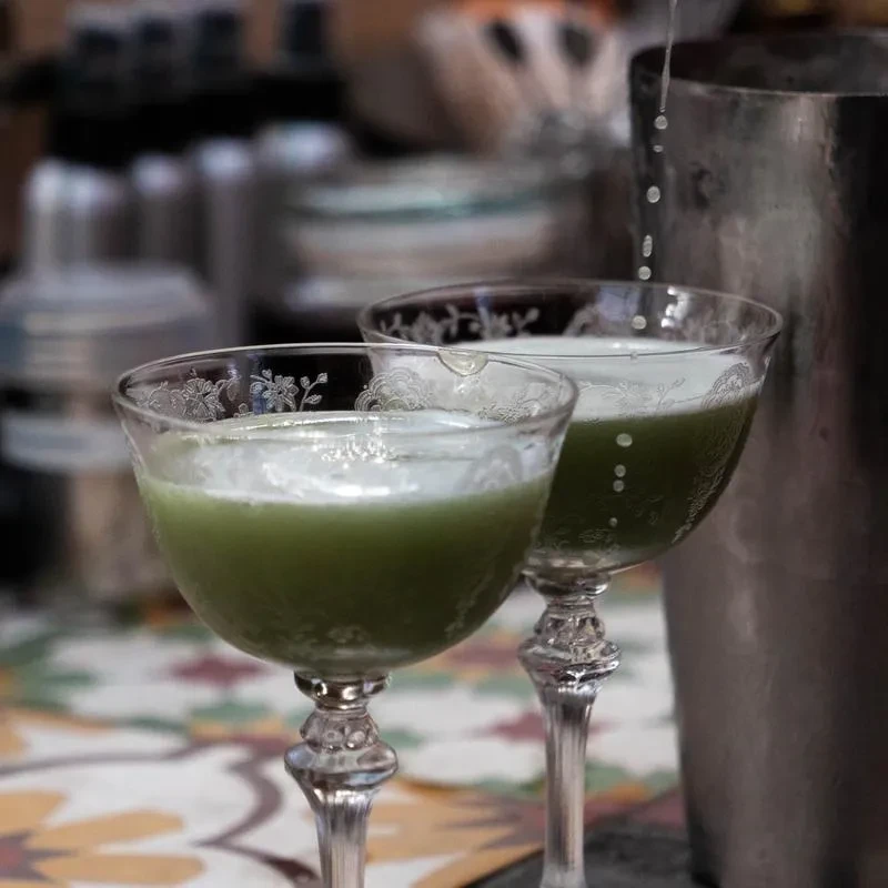 Two elegant etched glasses with green drinks, liquid pouring.