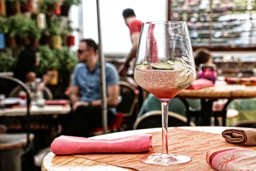 Pink sparkling drink in glass with cucumber on bright patio.
